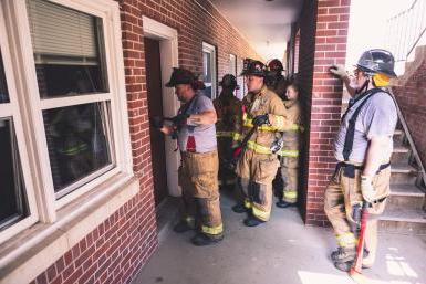 Firefighters watch a demonstration of breaking open a door outside of Burrage Hall. 